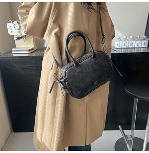 Close-up of black leather Boston bag with gold logo on a model in a trench coat
