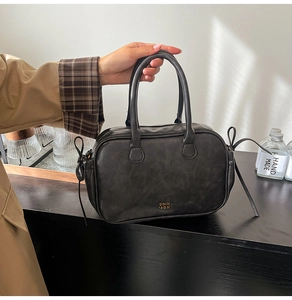 Detail of black matte Boston bag featuring top handles and lace-up side decorations