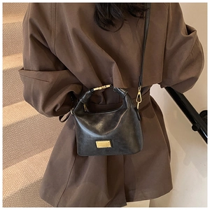 Close-up of black glossy leather handbag with gold metal hardware on model in trench coat
