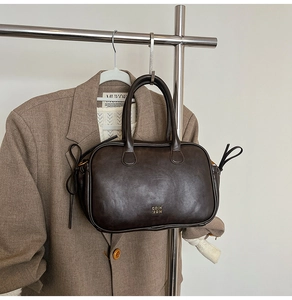 Detail of a dark brown leather Boston bag with gold logo hanging on a minimal metal rack