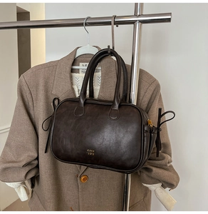 Detail of a dark brown vintage box bag with gold logo on a textured leather surface