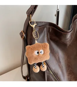 Close-up of a brown plush cartoon doll charm with gold keychain on a leather tote bag