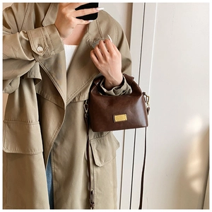 Detail of dark brown vintage faux leather handbag with golden metal plaque and slim strap
