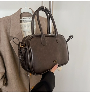 Detail view of coffee leather handbag featuring gold COIN 2DN logo and side drawstring