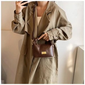 Detail of dark brown vintage dumpling bag with gold metal plate on khaki trench coat