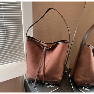 Detail of brown faux suede bucket bag featuring drawstring closure and slim shoulder strap