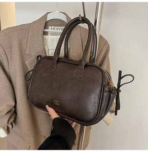 Detail of dark brown leather handbag featuring gold embossed lettering and side straps
