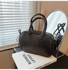 Detailed view of dark grey faux leather handbag with gold zipper and brand logo
