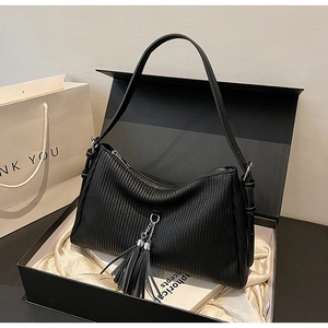 Detail of black pleated faux leather bag with large tassel pendant and silver chain