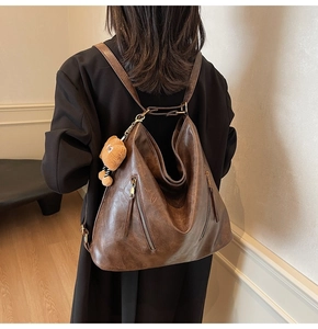 Macro detail of brown faux leather backpack featuring zipper pocket and bear plush charm