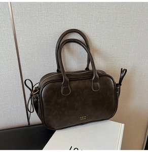 Detail of vintage dark brown handbag with dual handles and gold logo on textured leather