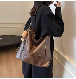 Detail view of brown PU leather tote bag with functional zippers and bear charm