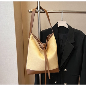 Close-up of beige canvas and brown leather tote bag styled with a black blazer
