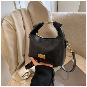 Detail of matte black handbag featuring knot handle design and gold metal hardware