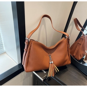 Close-up of brown pleated shoulder bag with fringe tassel and warm natural lighting