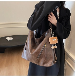 Detail of vintage brown leather tote with dual side zippers and a plush cartoon charm