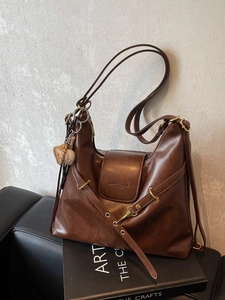 Bolso hobo retro de cuero marrón oscuro con colgante de béisbol en sofá de cuero