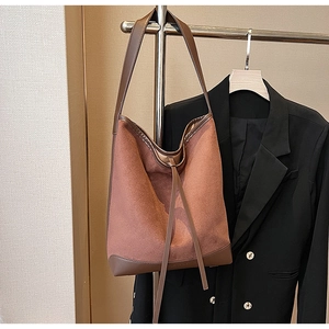 Brown matte suede bucket bag with leather trim hanging on a rack with a black blazer