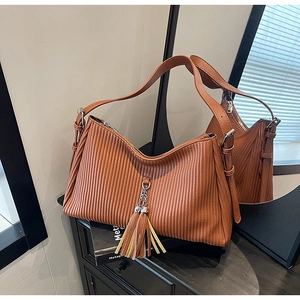 Detailed macro view of brown pleated faux leather shoulder bag with long tassel and chain