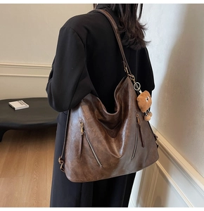 Detail view of large dark brown tote bag with retro leather texture and plush bear charm
