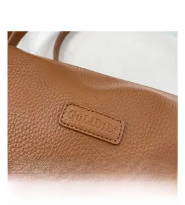 Macro detail of brown pebbled leather bag with fine stitching and embossed logo tag