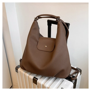 Bolso tote marrón grande de estilo vintage sobre una maleta blanca para viajar.