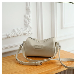 Detailed view of beige cylinder crossbody bag with GULIDISI logo and litchi texture