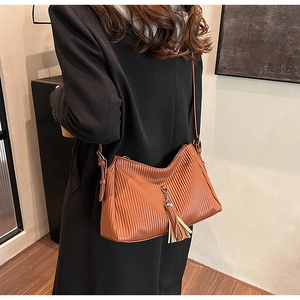 Detail of a brown shoulder bag with pleated texture and tassel charm on a model