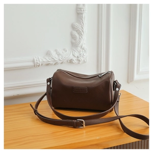 Detail of dark brown pebble leather texture and metal buckle on the cylinder bag