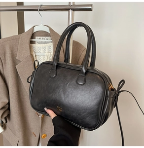 Detail of a vintage black leather handbag with gold logo shown in a lifestyle outfit setting
