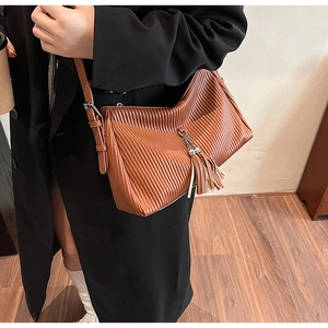 Detail of pleated texture on a brown faux leather shoulder bag with fringe tassel charm