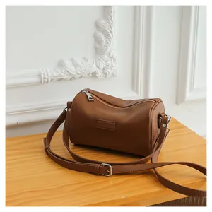 Detail of dark brown lychee leather cylinder bag with adjustable shoulder strap and logo