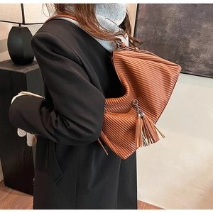 Detail of caramel brown pleated leather shoulder bag with side tassel metallic accents