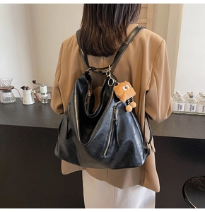 Detail of black soft leather backpack with functional zippers and cute plush charm pendant