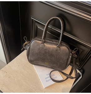 Detailed view of dark grey retro handbag with gold logo on beige stone surface