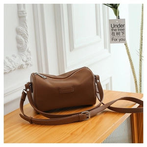 Close-up of brown pebbled leather texture and brand embossing on the cylindrical pillow bag