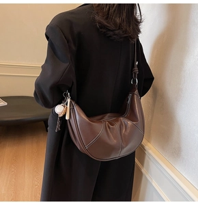 Detail of dark brown leather crescent bag with white stitching and baseball charm on a model