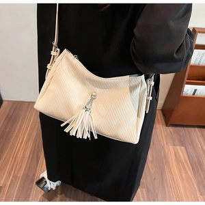 Detail of cream pleated crossbody bag featuring a long tassel with metal ring