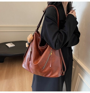 Detail of a brown leather tote bag with parallel zippers and a cute bear charm accessory