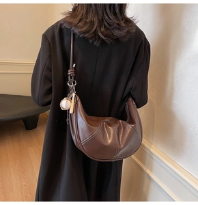 Detail of dark brown crescent bag with white contrast stitching and baseball charm