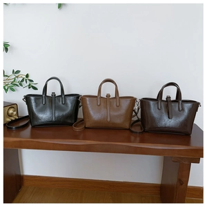 Trois sacs seaux vintage en similicuir noir, marron et café posés sur un banc en bois