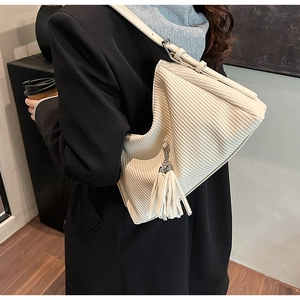 Detail of cream pleated shoulder bag with tassel and adjustable strap on a model