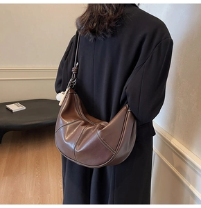 Detail of a brown leather crescent hobo bag with white stitching on a shoulder strap