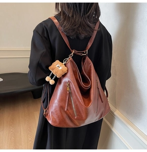 Detail of a brown PU leather backpack with zippers and a cute plush bear charm on a model