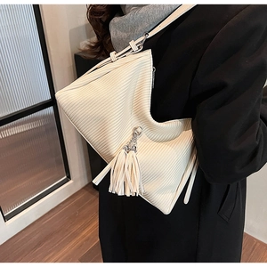 Detail of a creamy white tote bag with vertical textures, leather strap, and long tassel