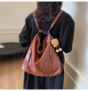 Detail of brown vintage leather backpack with vertical zippers and plush charm