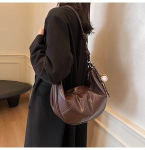 Detail of dark brown leather crescent bag with white stitching and knot strap on model