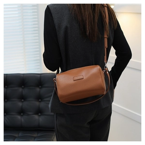 Detail of a brown leather cylinder crossbody bag featuring pebbled texture and logo patch