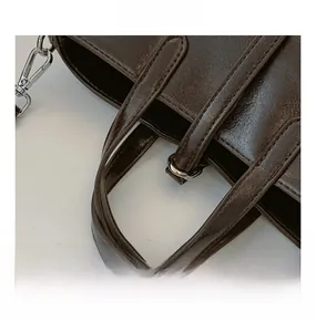 Détail des poignées cousues et des ferrures métalliques argentées sur un sac marron foncé
