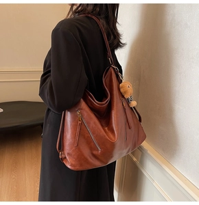 Brown tote bag detail with side pocket and plush bear pendant hanging from wide strap